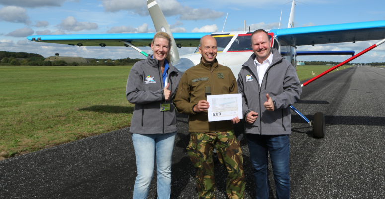 Wendy (links) en Emile (rechts, piloot ambulancevliegtuig) ontvangen van Kapitein J. Tokaya van het 931 Squadron de cheque op Gilze-Rijen.